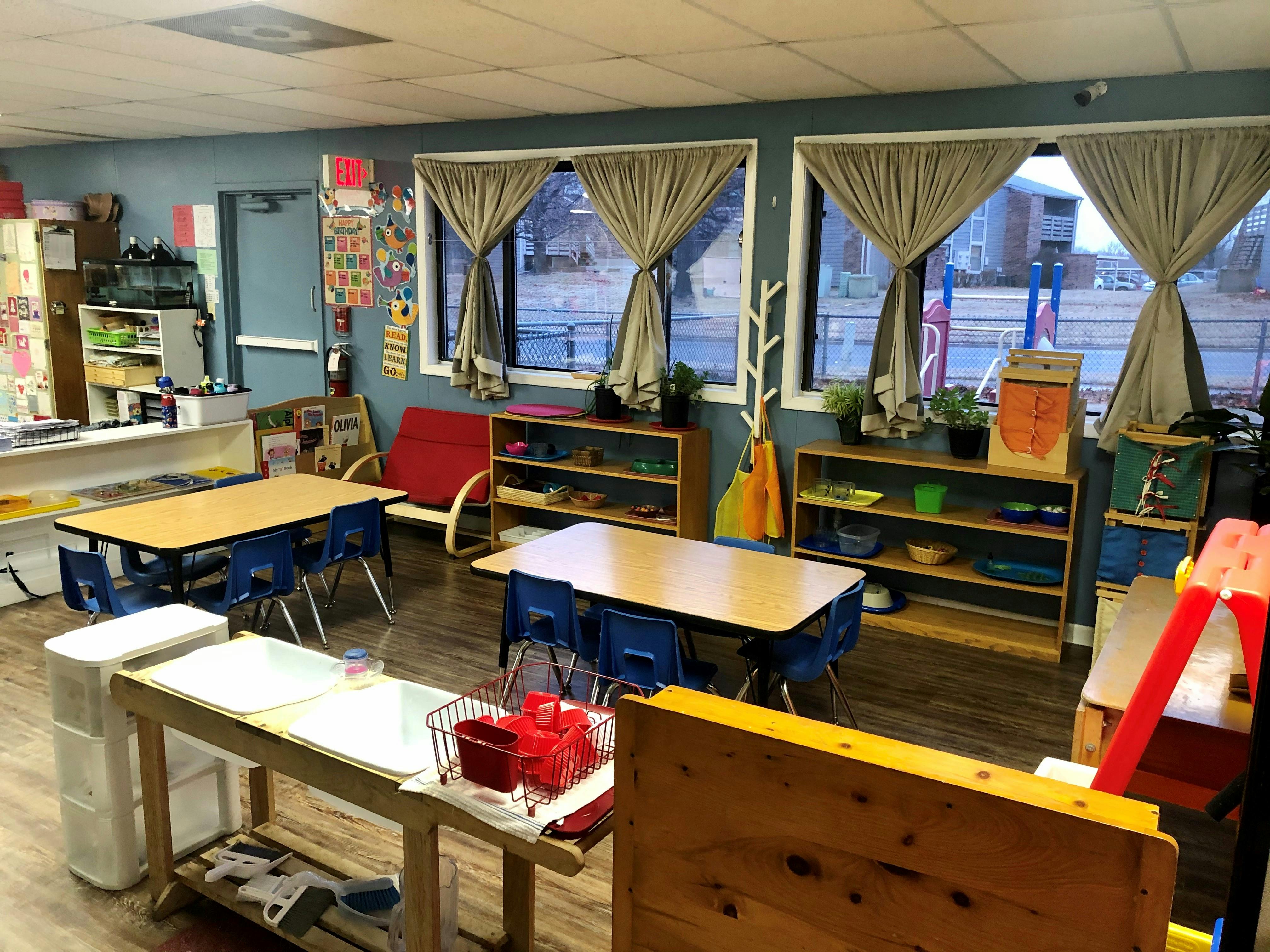 Classroom with small tables and chairs, shelves, and large windows