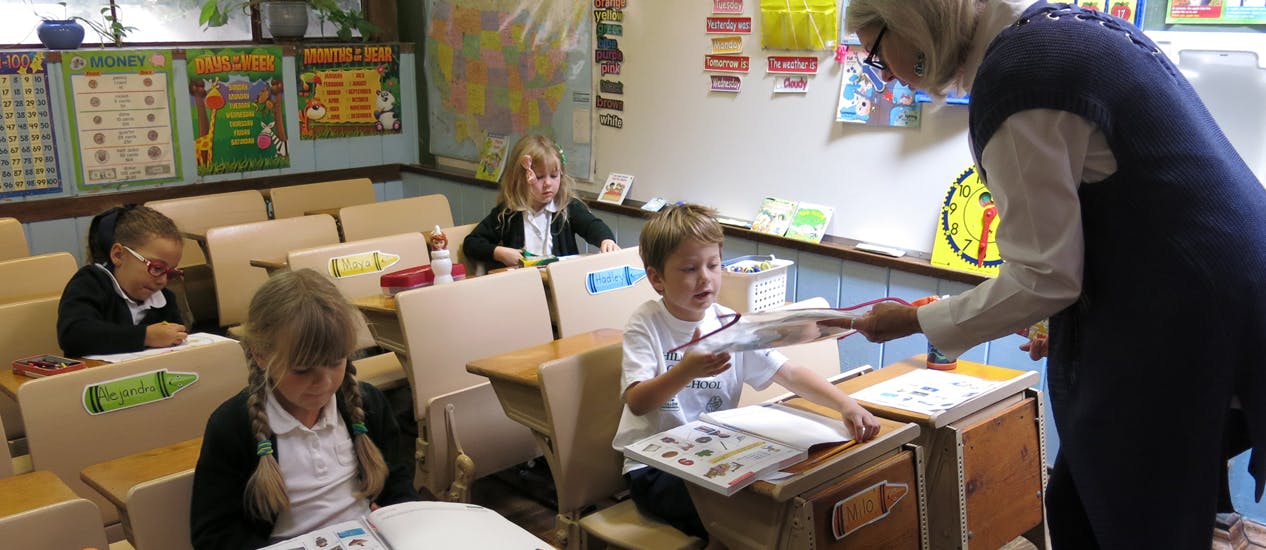 Teacher handing papers to a child in a classroom with other children