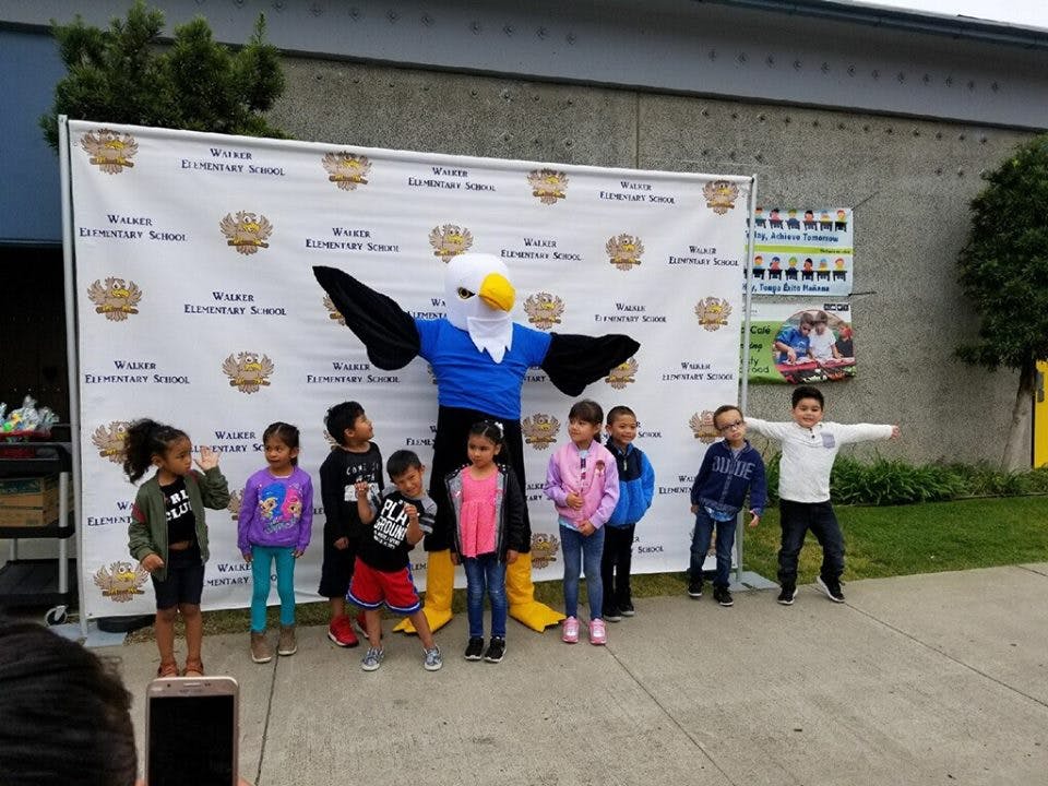 Mascot in eagle costume with children standing in front of a banner