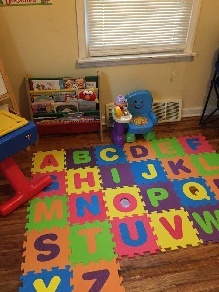 Alphabet playmat on a wooden floor in a room with a bookshelf and toys