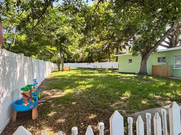 Spacious grassy backyard with white fences and water play toys