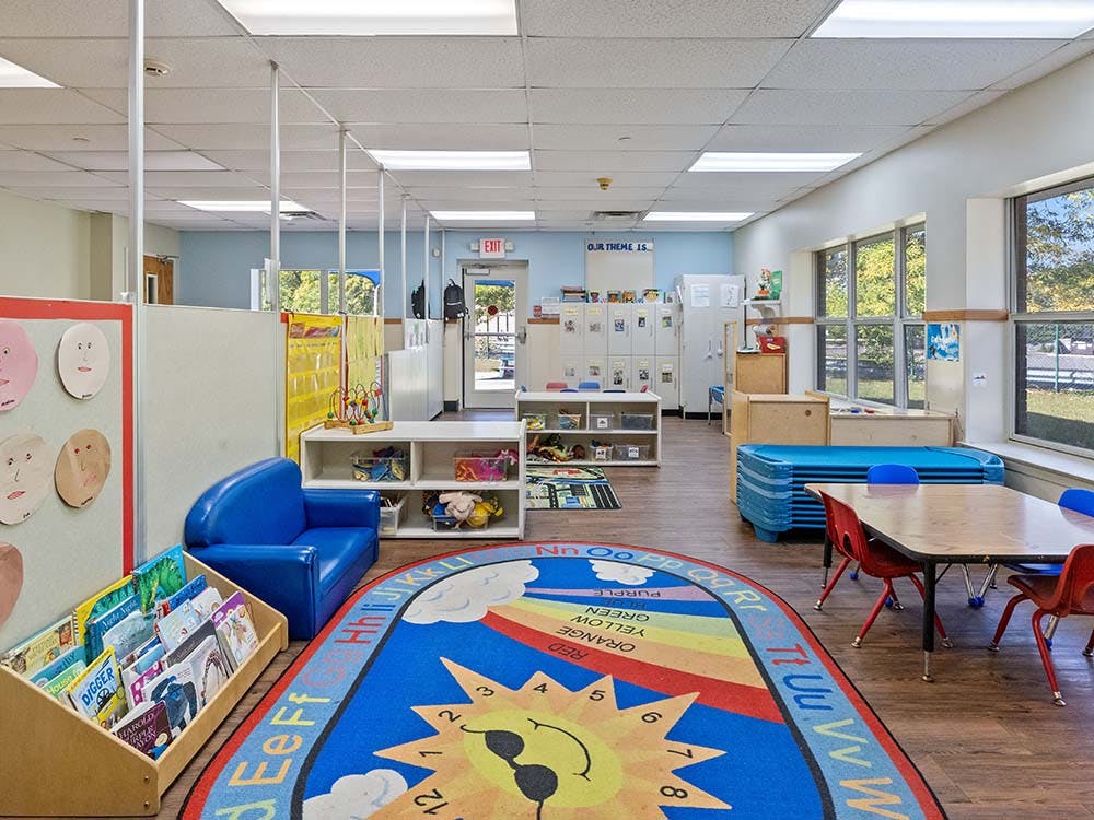 daycare classroom with a colorful rug, tables, chairs, and shelves of toys