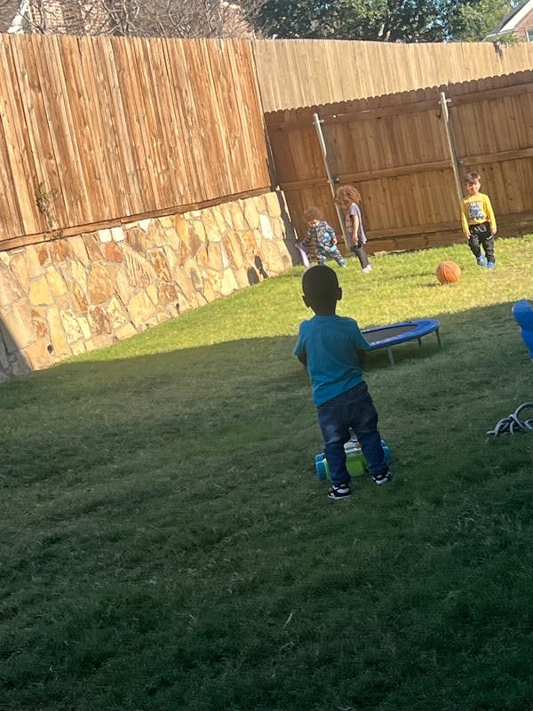 Children playing in a grassy backyard with a trampoline and a ball