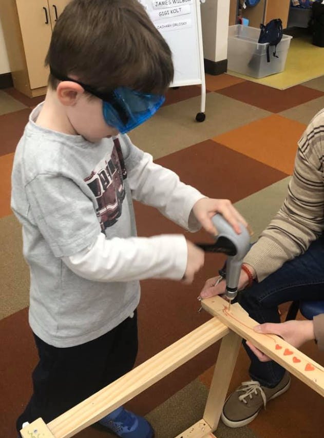 Child wearing safety glasses using a drill on a wooden frame