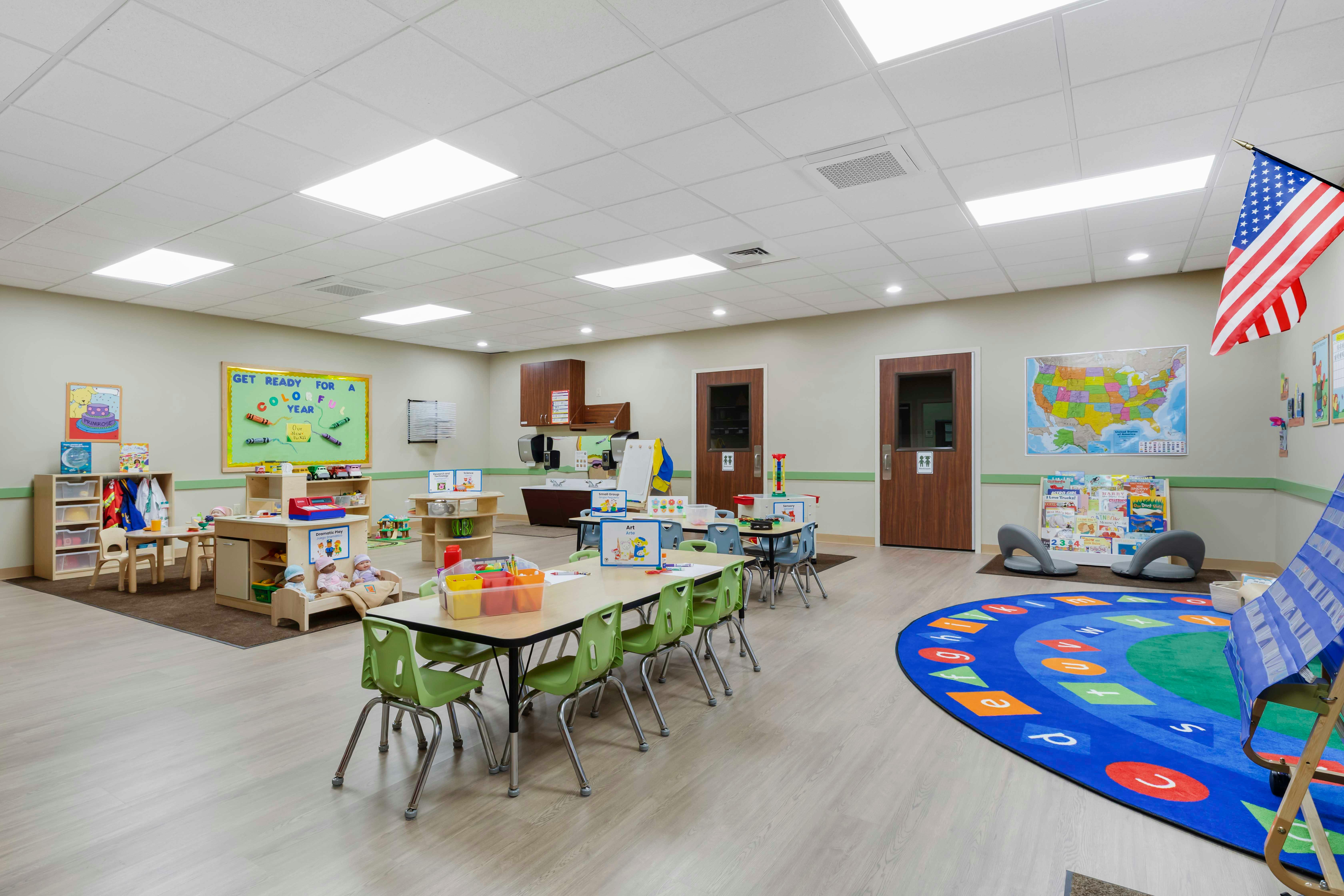 Classroom with small tables and chairs, a play area, and an American flag
