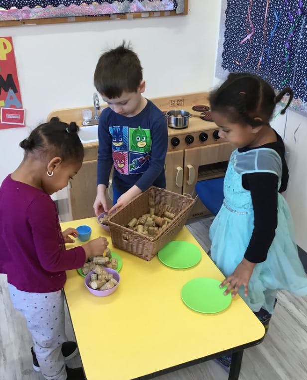 Three children playing with items on a yellow table in a classroom