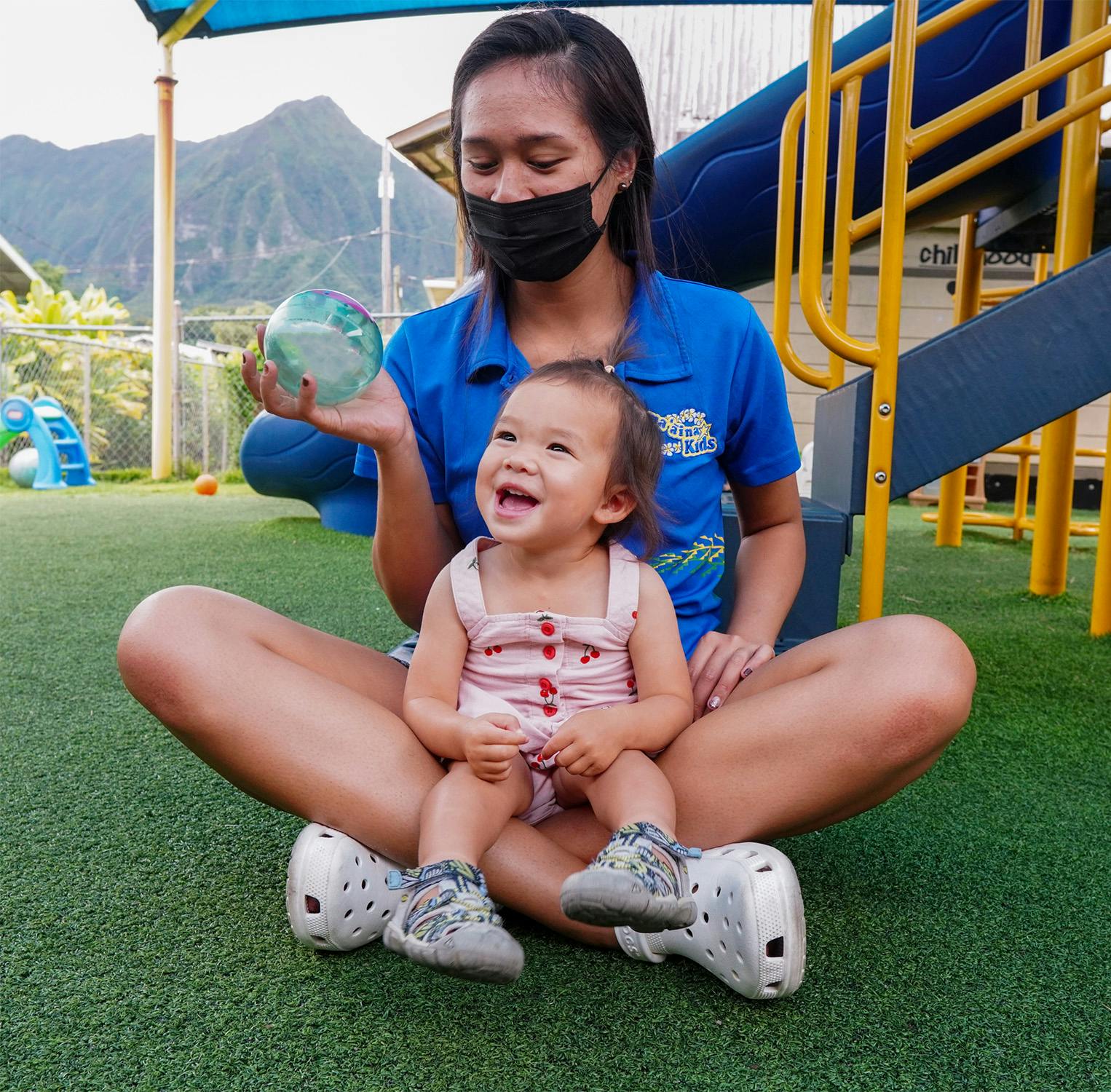 Person in mask holding a clear ball with a child sitting on their lap