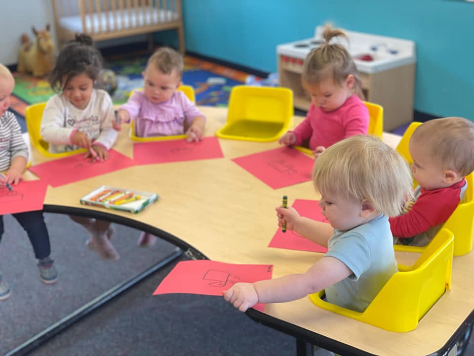 Children sitting at a table coloring on red paper