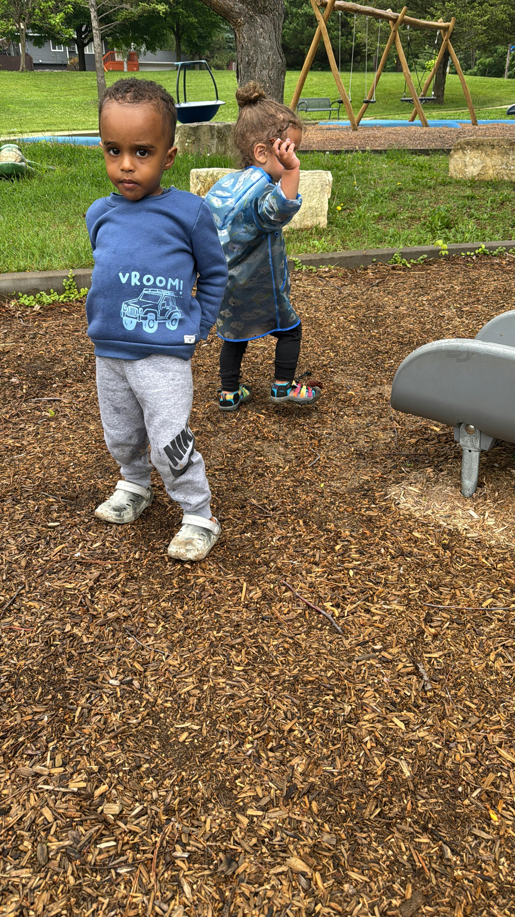 Two children standing on wood chips in a playground