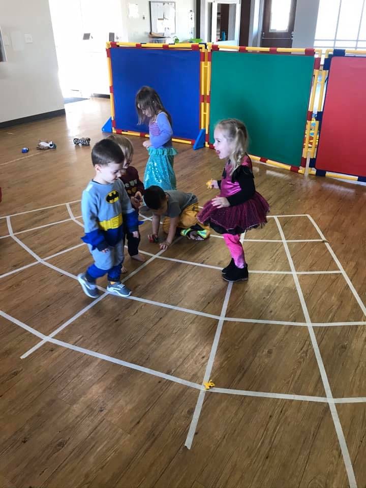 Children playing on a grid of tape on a wooden floor