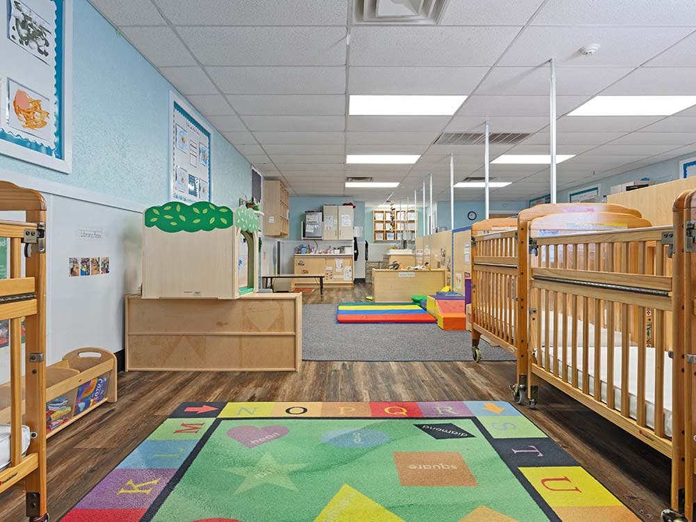 Classroom with wooden cribs, play rug, and light blue walls