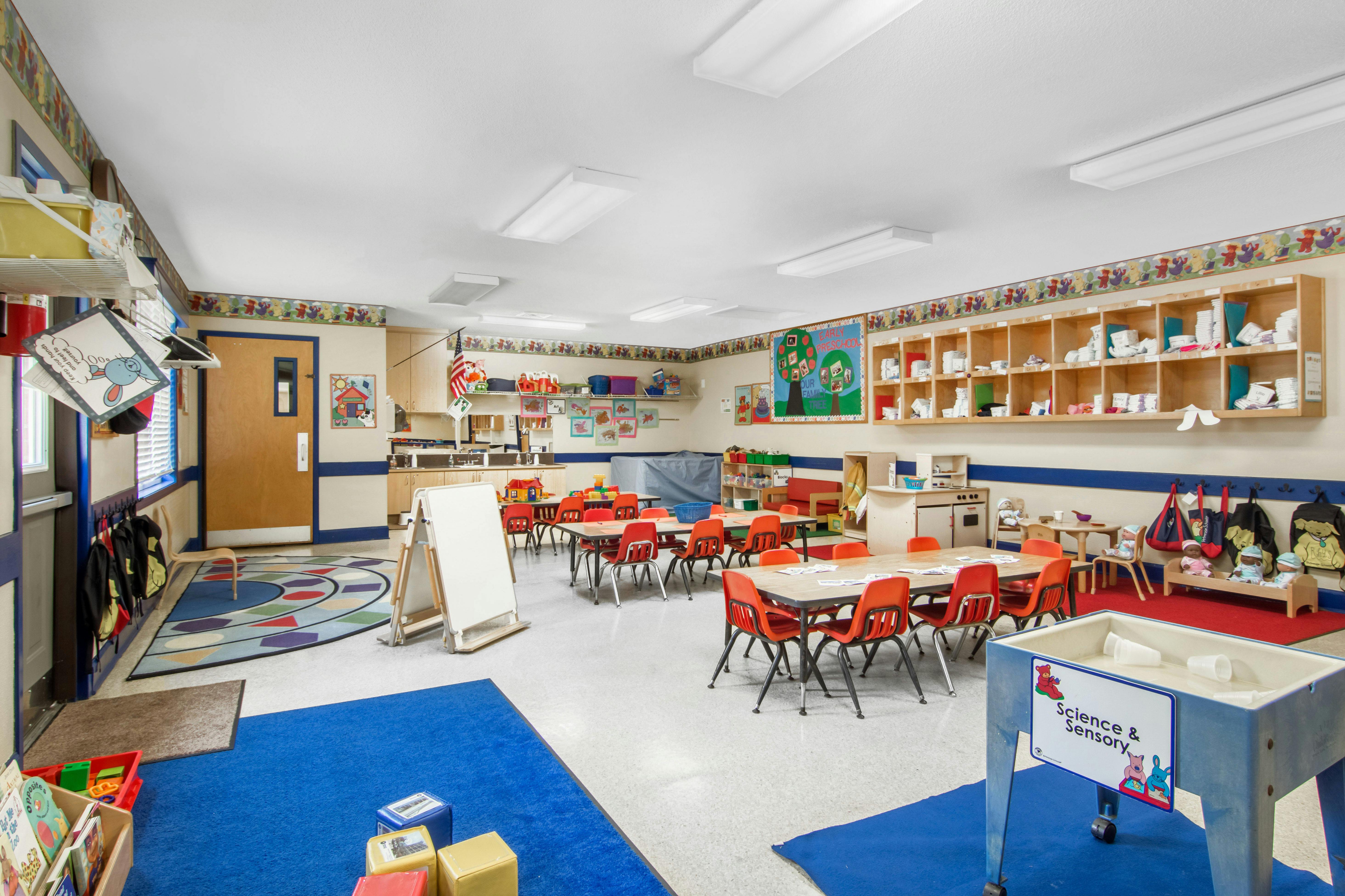 Classroom with small tables and chairs, play kitchen, and sensory table