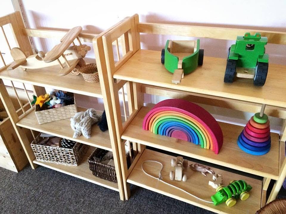 Wooden shelves with various toys including a rainbow stacker and wooden vehicles