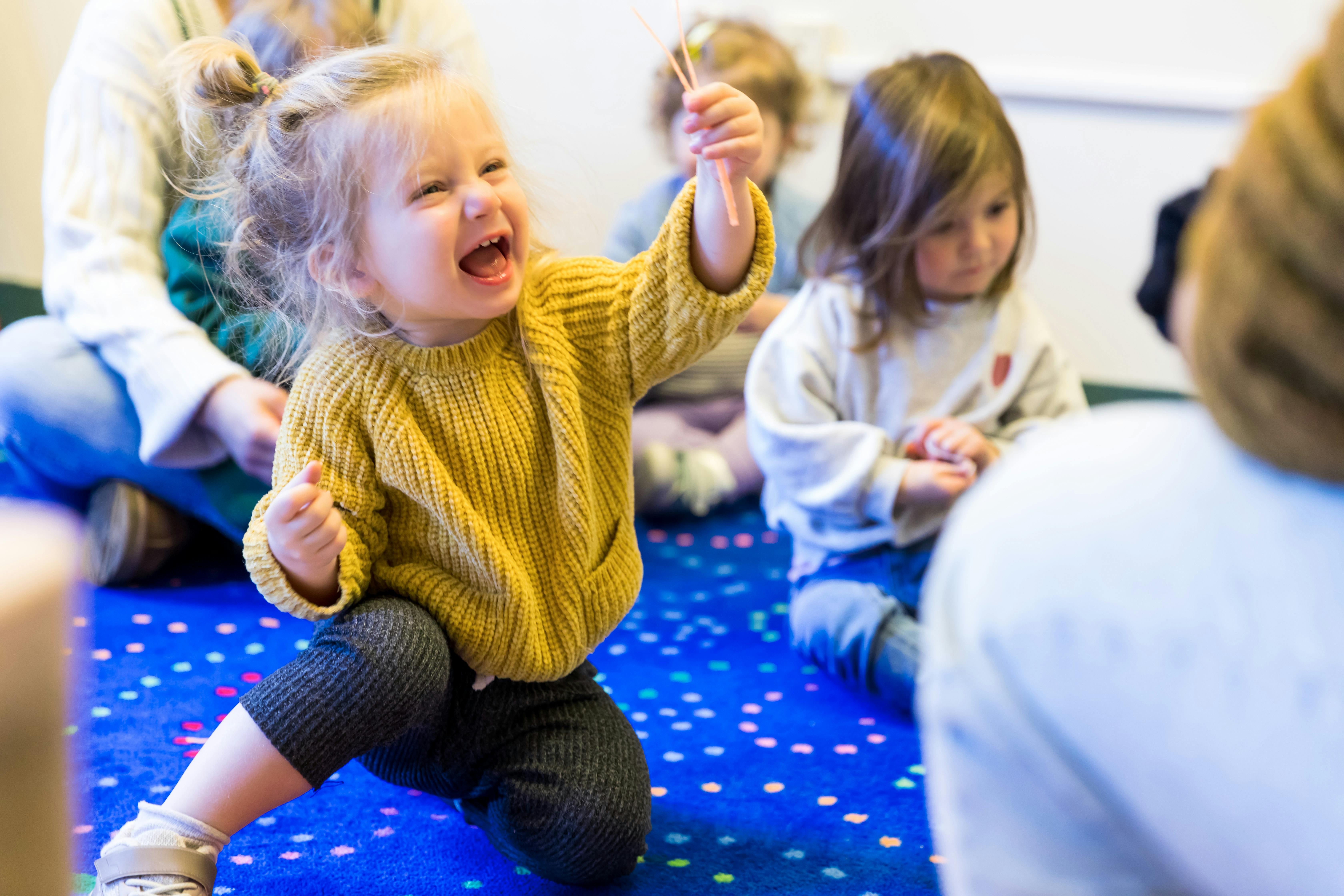 Child in yellow sweater kneeling on blue floor with other children
