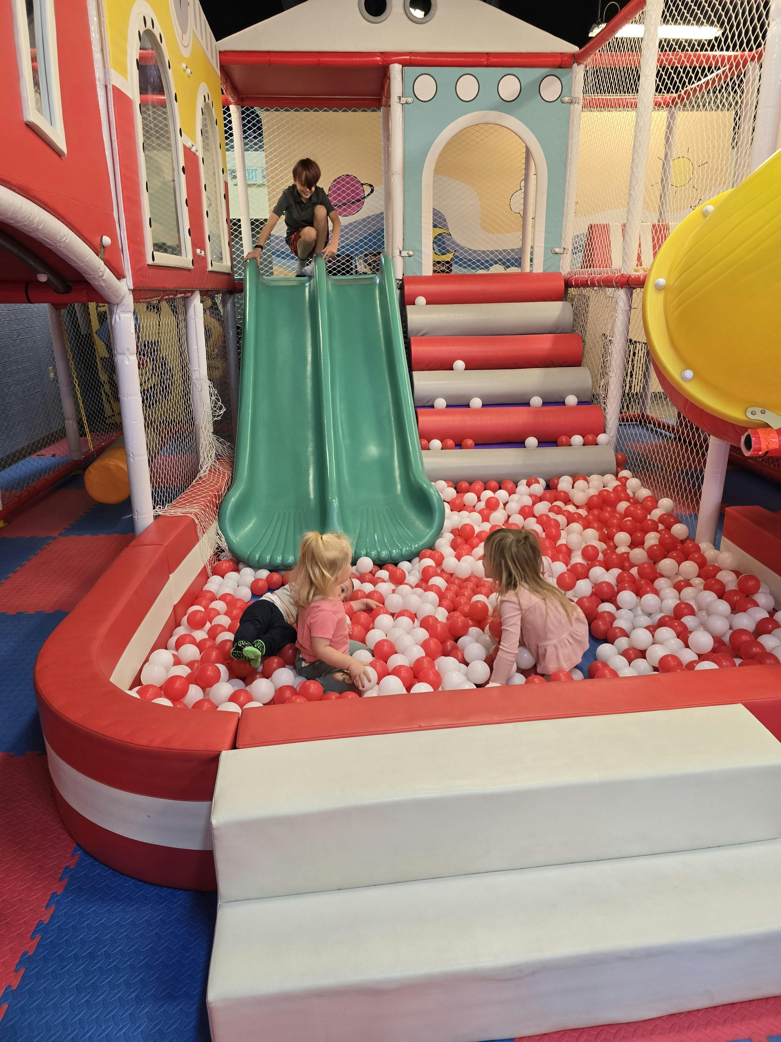 Child on top of a slide and two children in a ball pit
