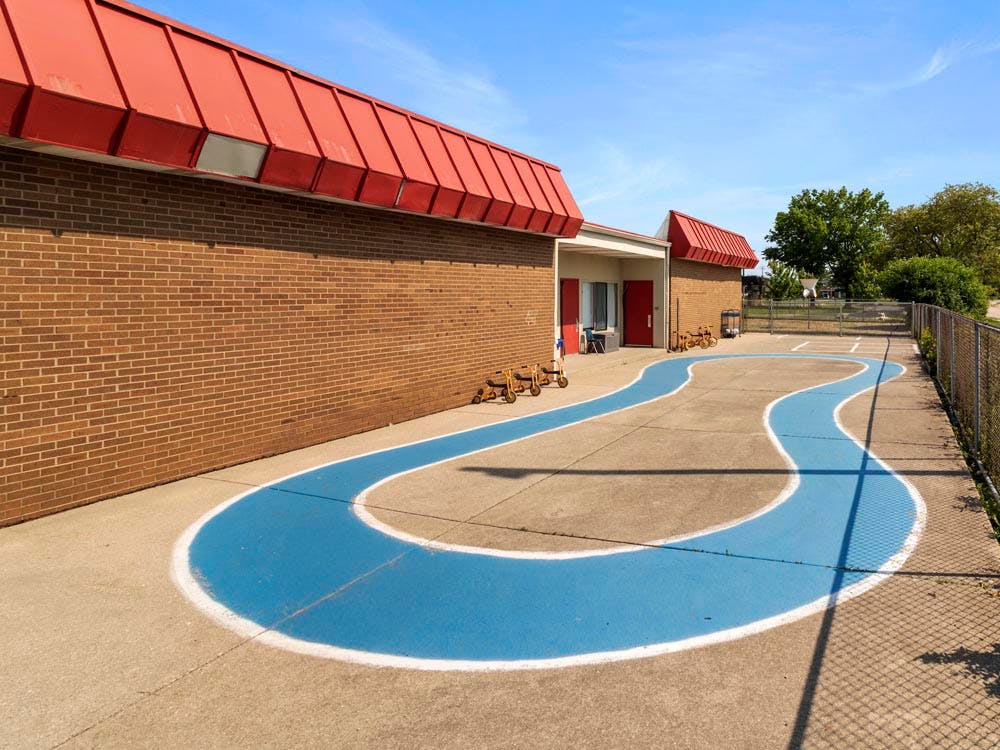 Playground with blue painted path and tricycles next to a brick building