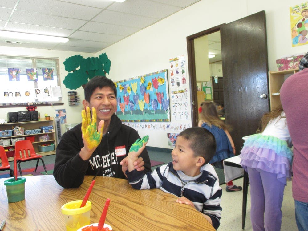 Person and child with painted hands in a classroom