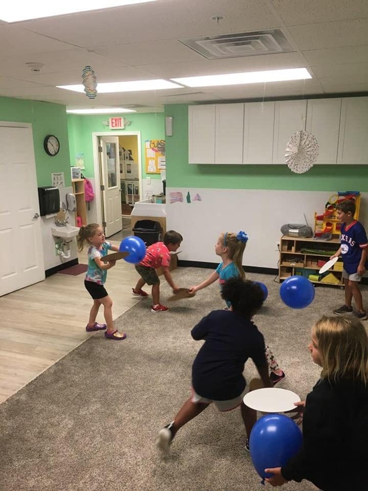 Children playing with balloons and paddles in a classroom