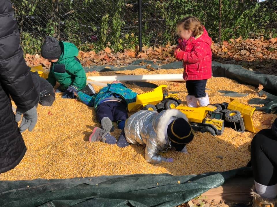 Children playing in a corn pit with toy construction vehicles