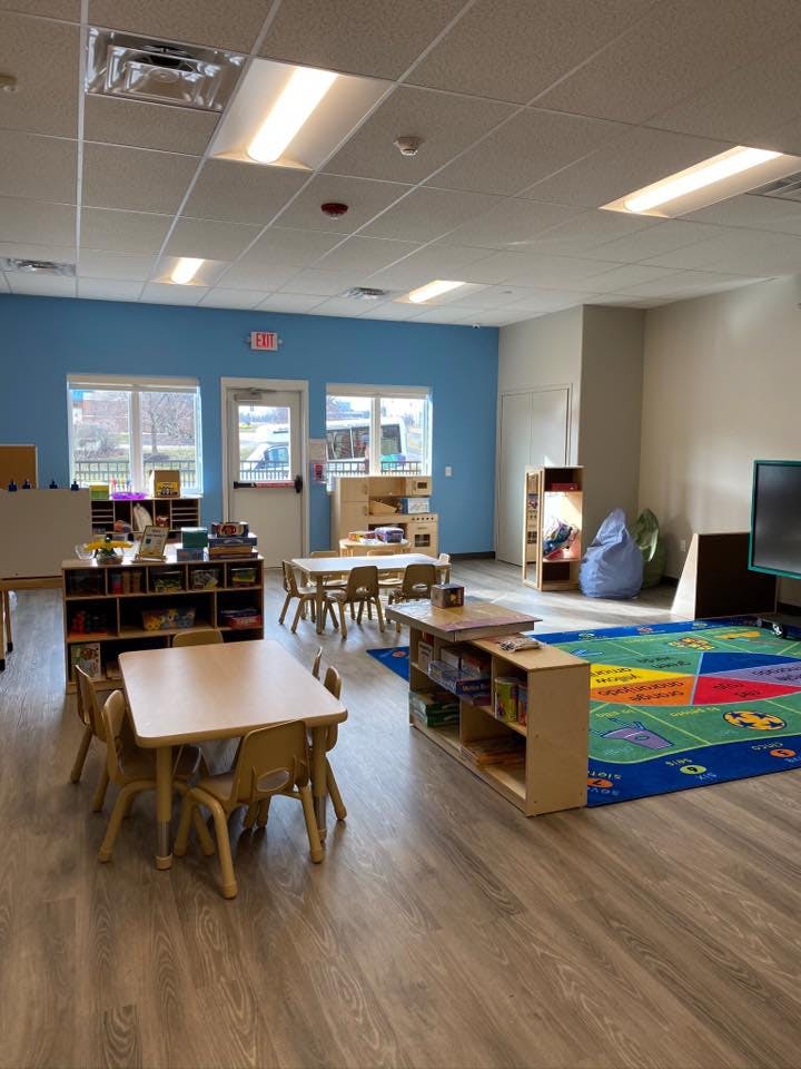 Classroom with small tables and chairs, shelves, and a colorful rug