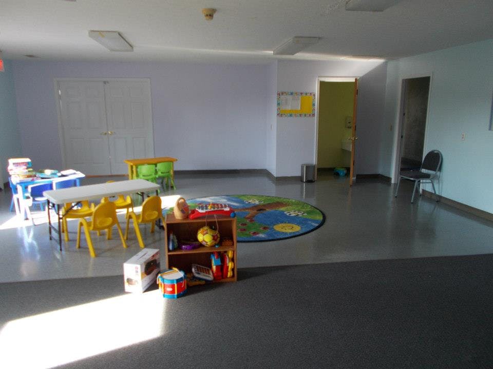 Empty classroom with small tables, chairs, and a round rug