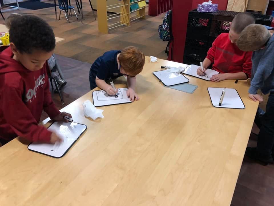 Four children writing on whiteboards at a table
