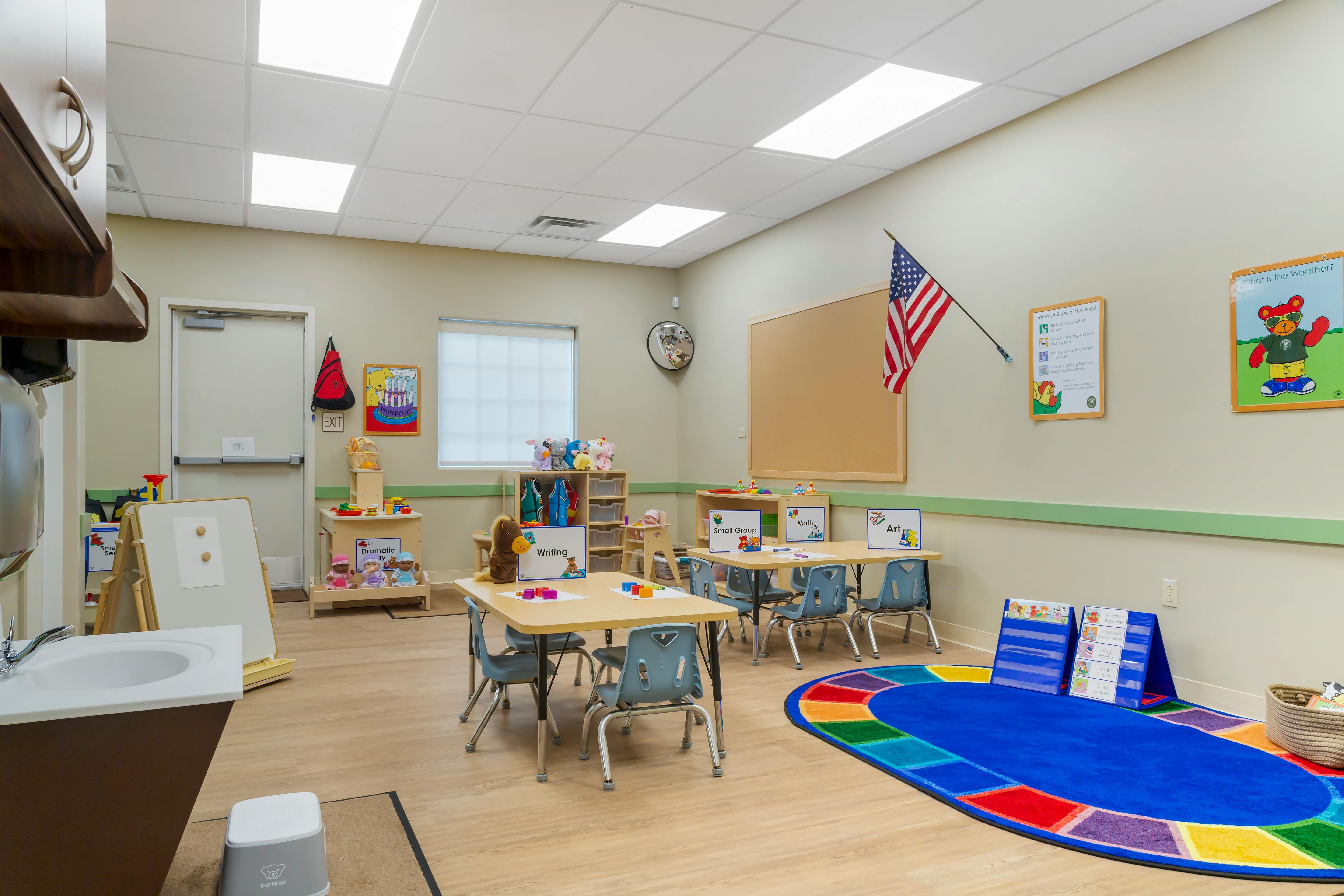 Classroom with child-sized tables and chairs, a sink, and colorful rug