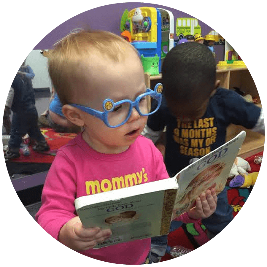 Child in blue glasses reading a book with another child