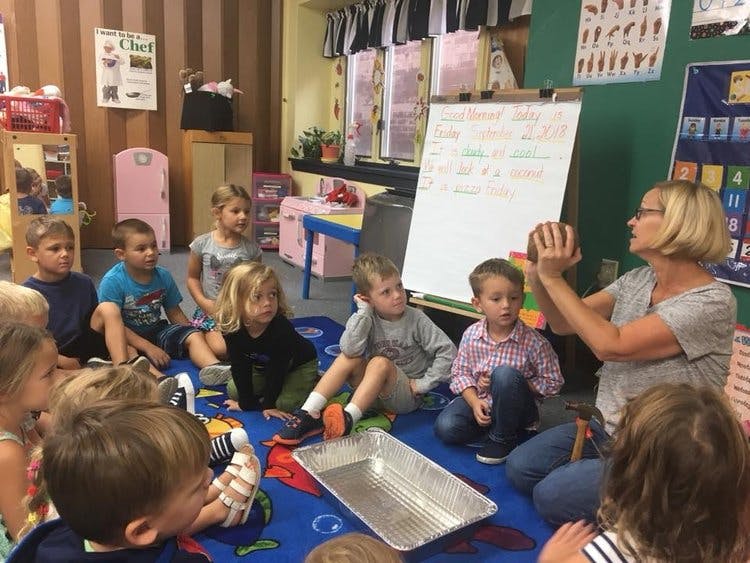 Adult person showing an object to a group of children in a classroom