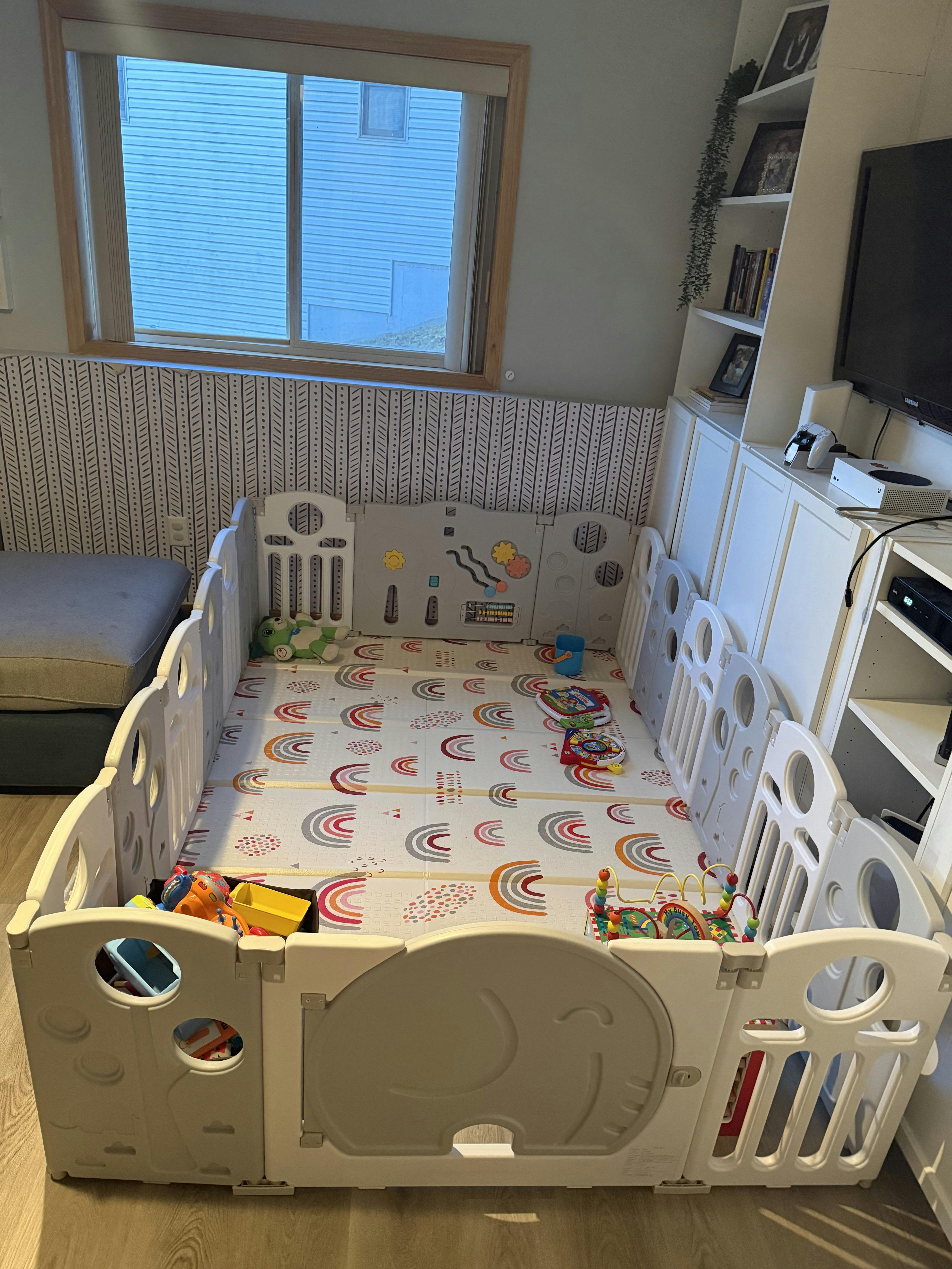 A baby playpen with a colorful rainbow mat and toys inside