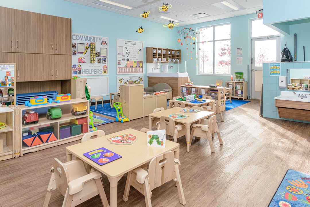 Classroom with small wooden tables and chairs, toys on shelves, and wall decorations