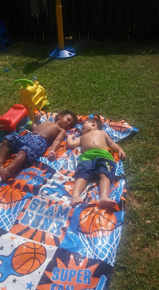Two children lying on a basketball-themed blanket on grass