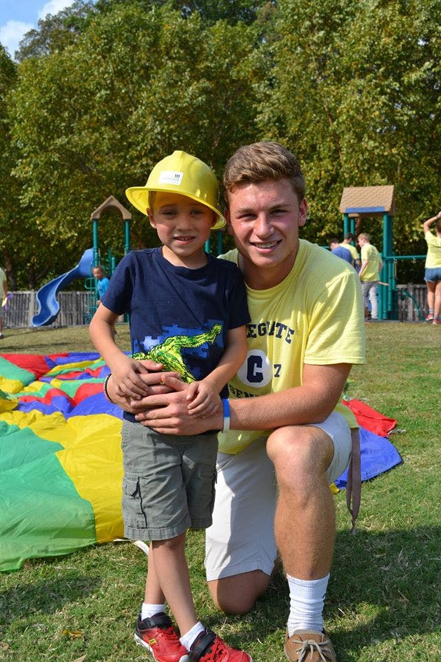 Adult person kneeling next to a child wearing a yellow hat