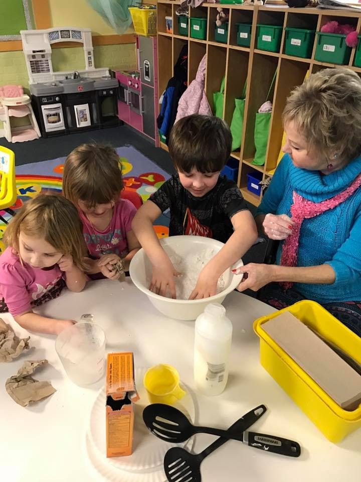 Adult and three children playing with dough in a bowl