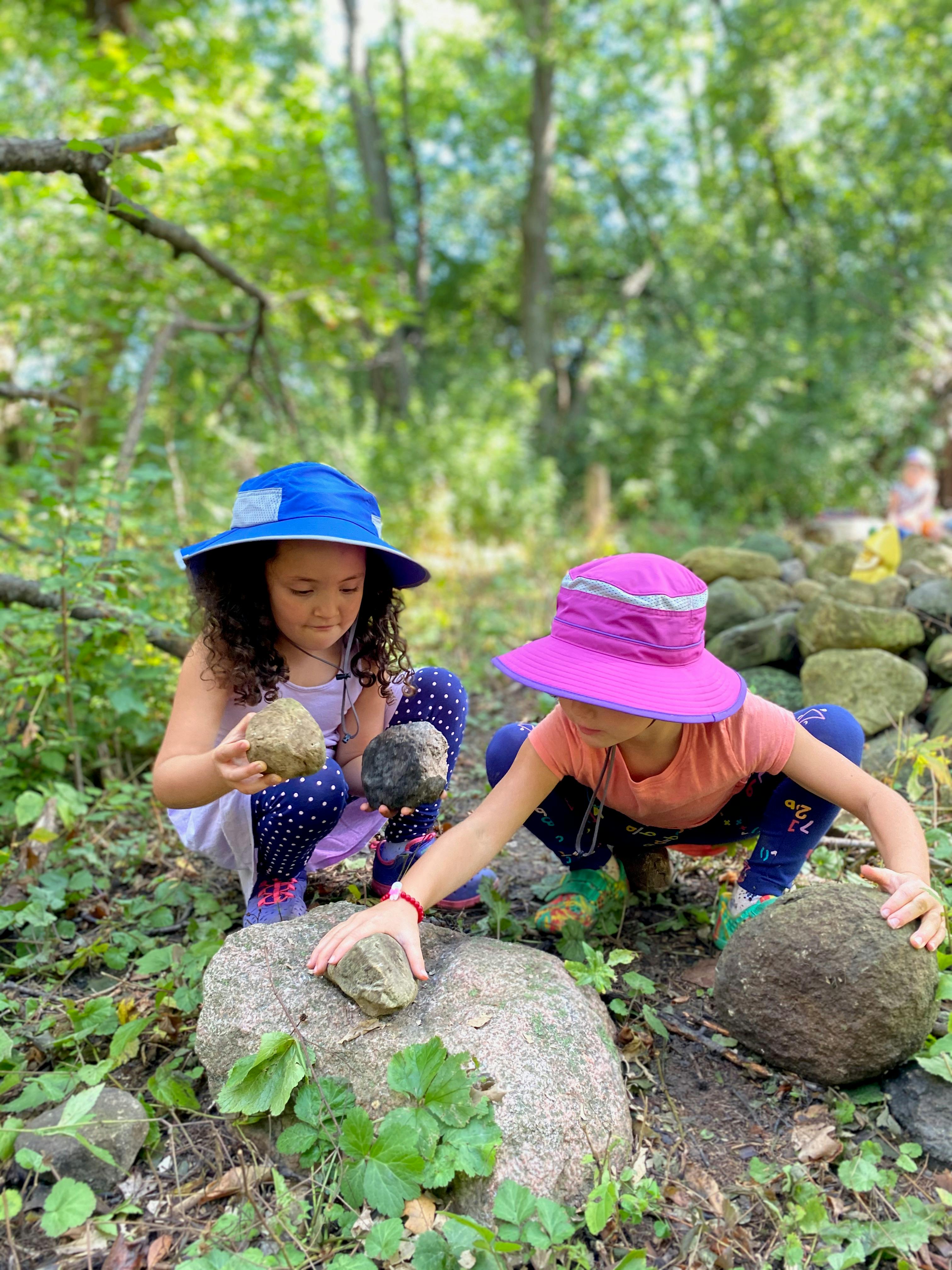 Two children in hats playing with rocks outdoors