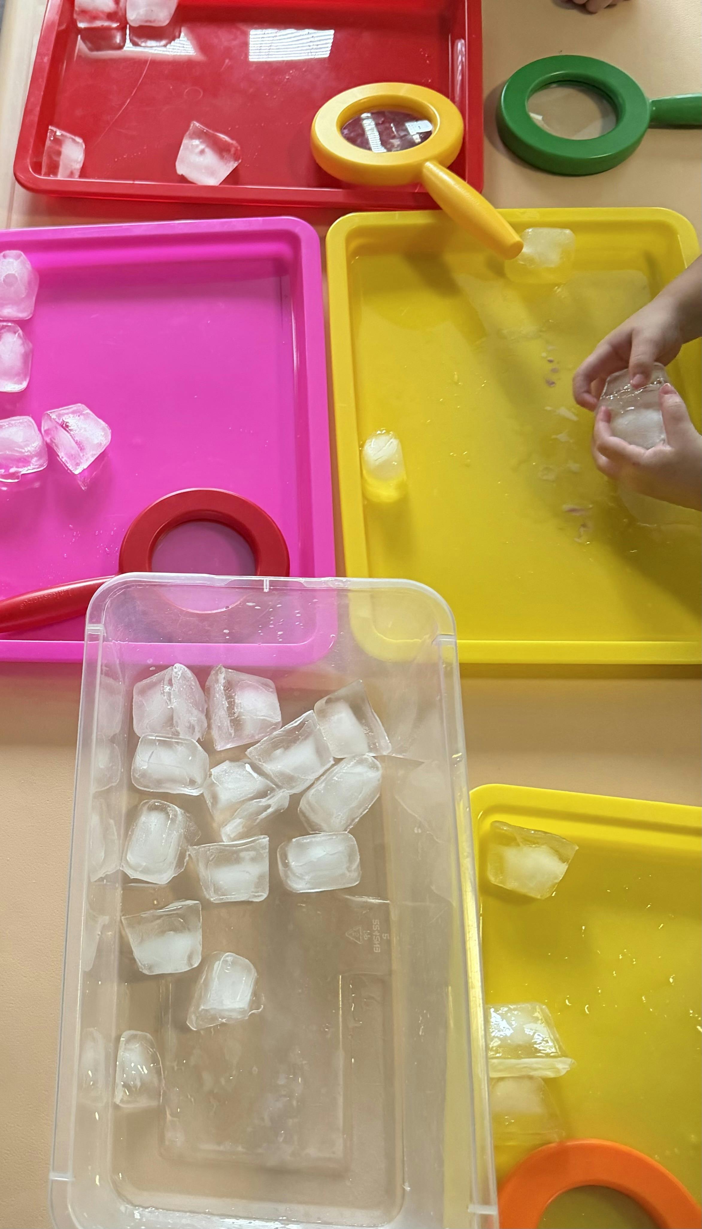 Child's hands playing with ice cubes and colorful trays