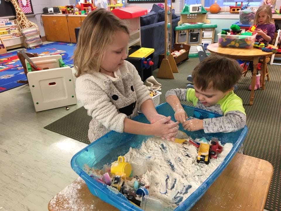 Two children playing with toys in a sensory bin filled with white material