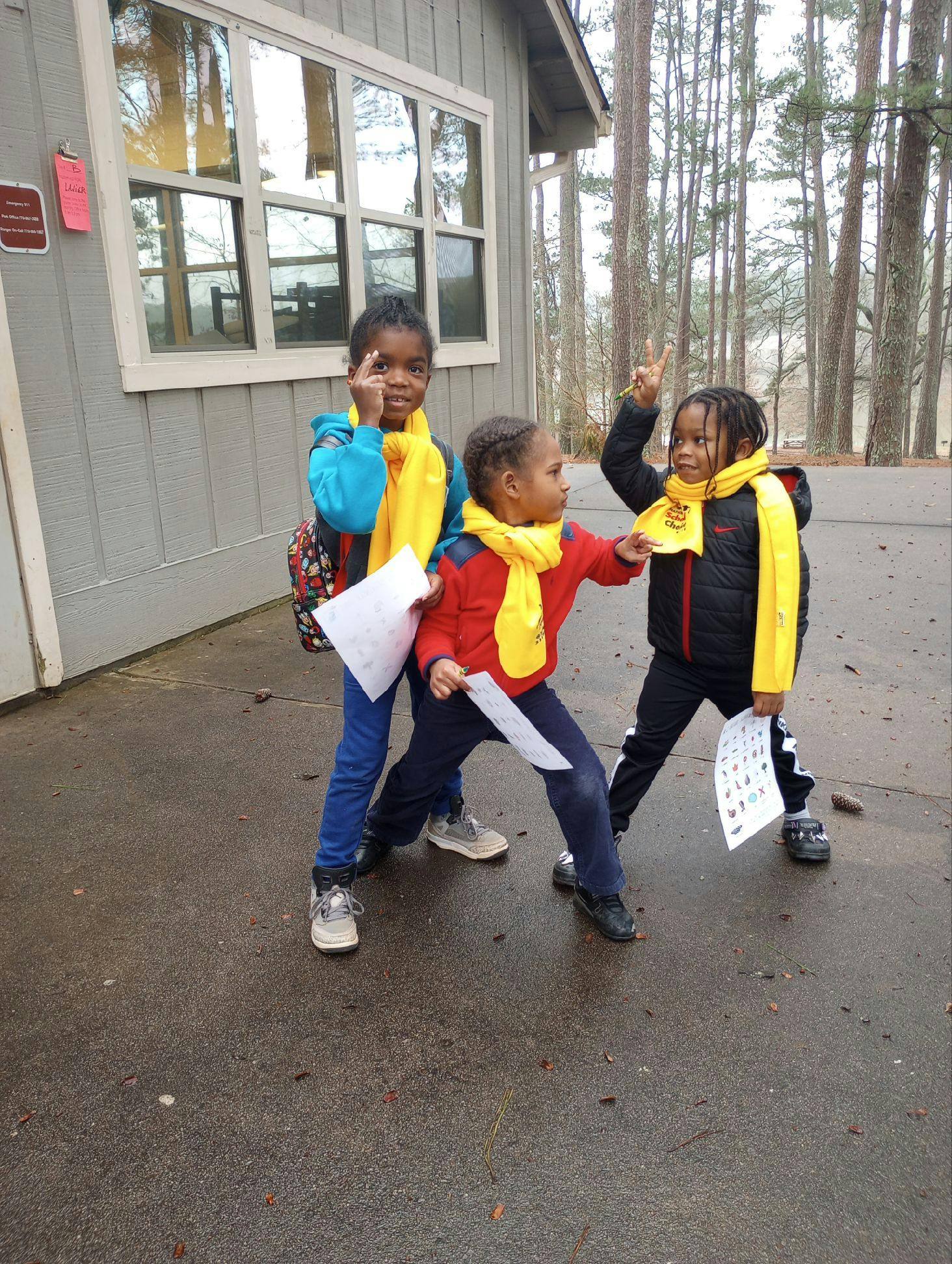 Three children in yellow scarves holding papers and pointing
