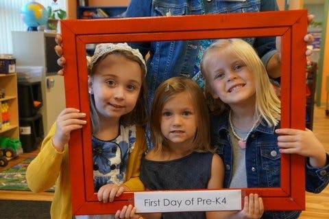 Three children holding a red frame with "First Day of Pre-K4" sign
