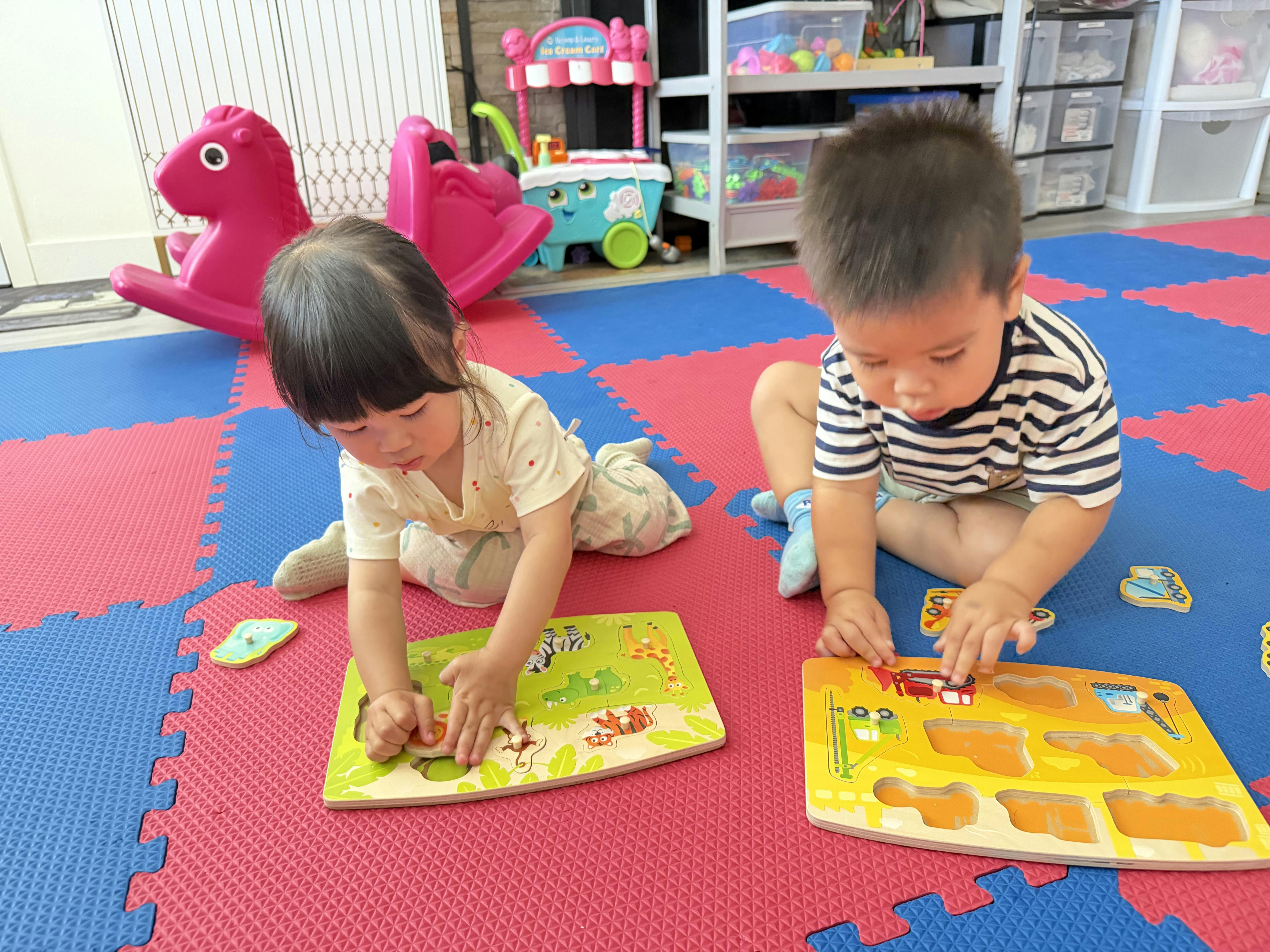 Two children sitting on a play mat assembling wooden puzzles