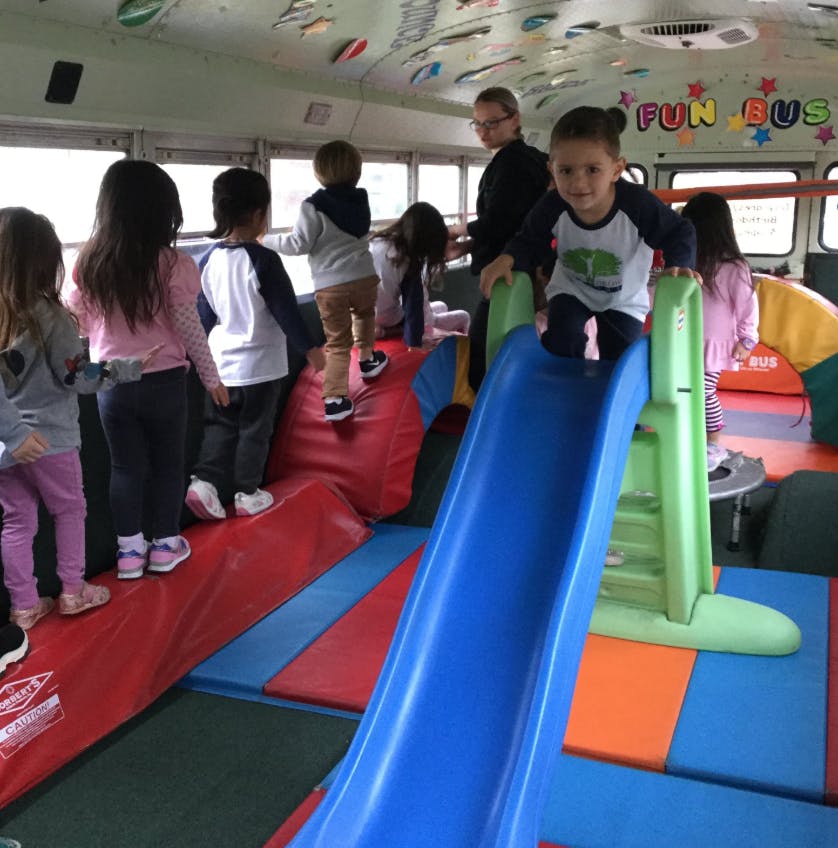 Child on a blue slide with other children and an adult in a play area