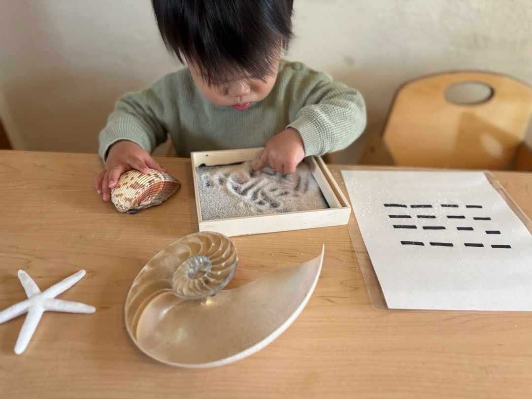 Child playing with sand tray and shells on a wooden table