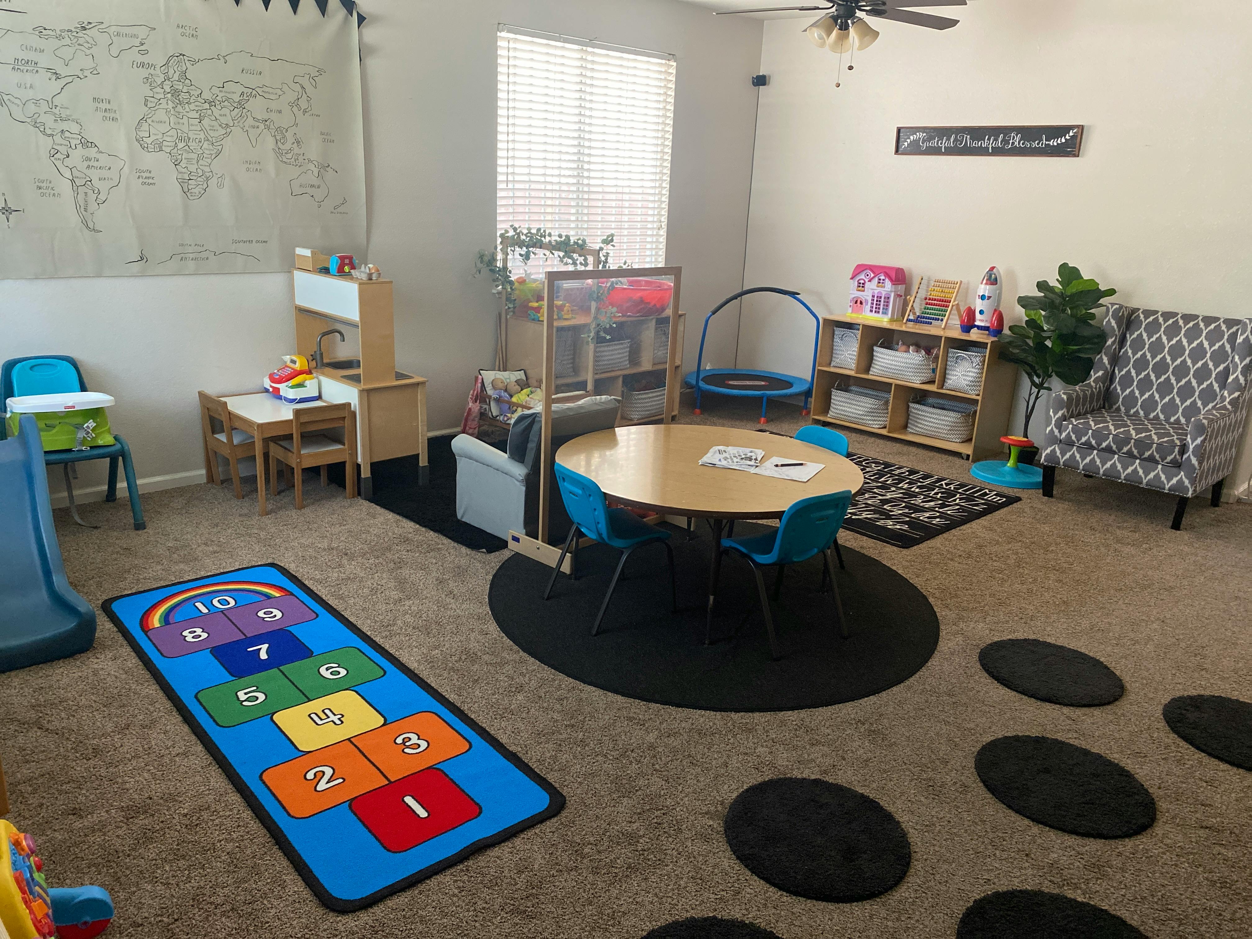 Playroom with small tables, chairs, and a hopscotch rug