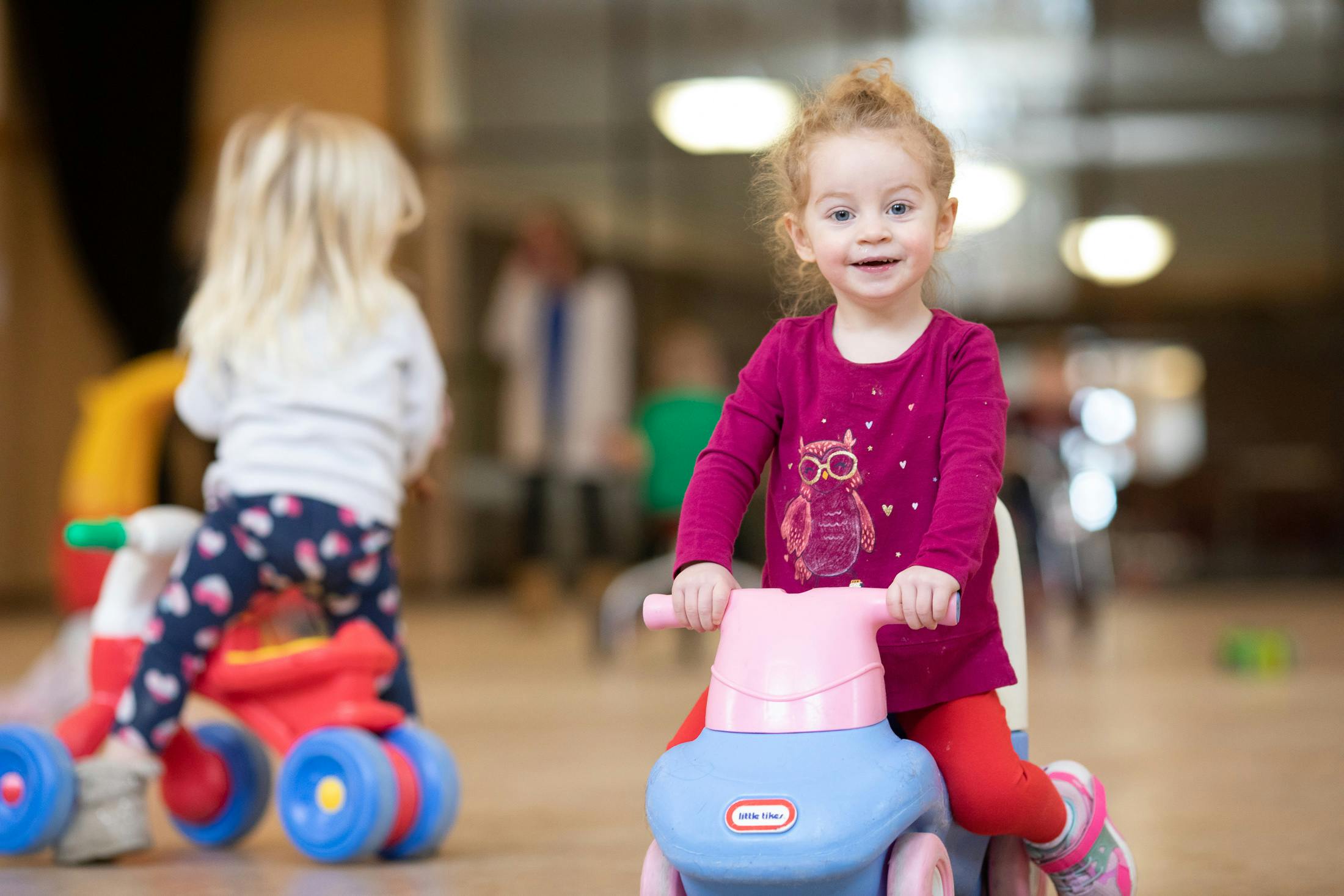 Two children riding toy bikes indoors