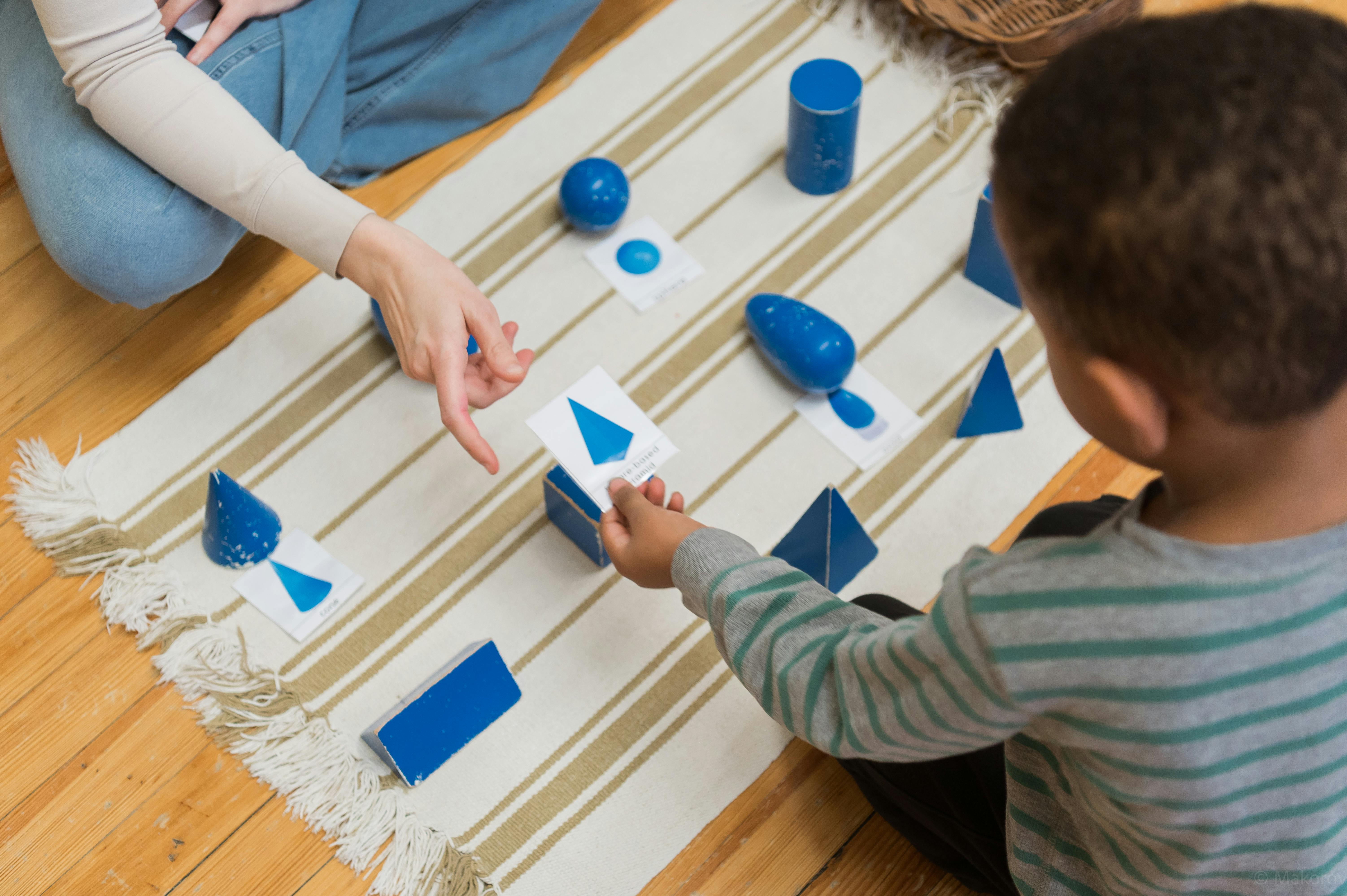 Person and child playing with blue geometric shapes and cards on a rug