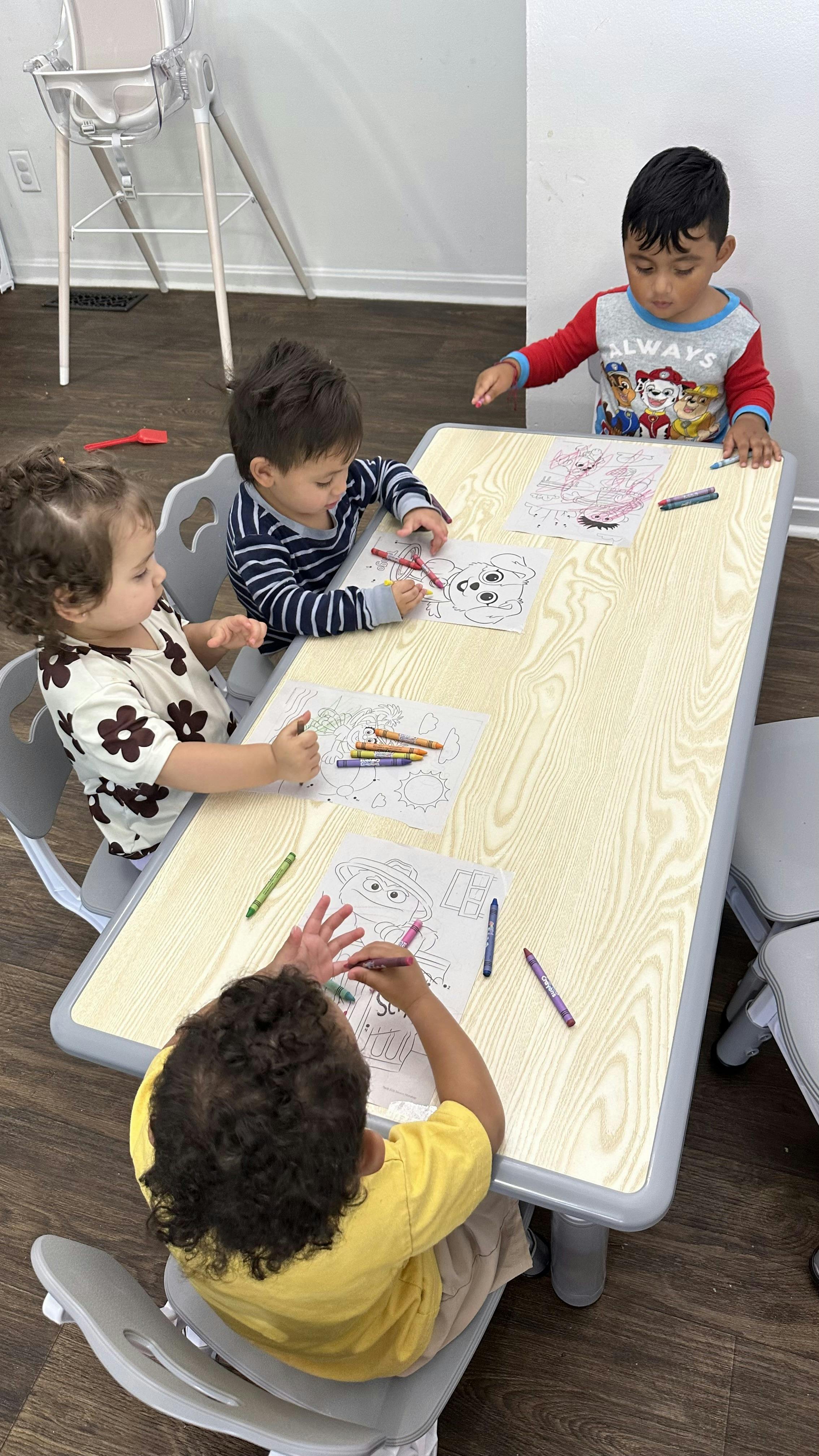 Four children sitting at a table coloring on paper