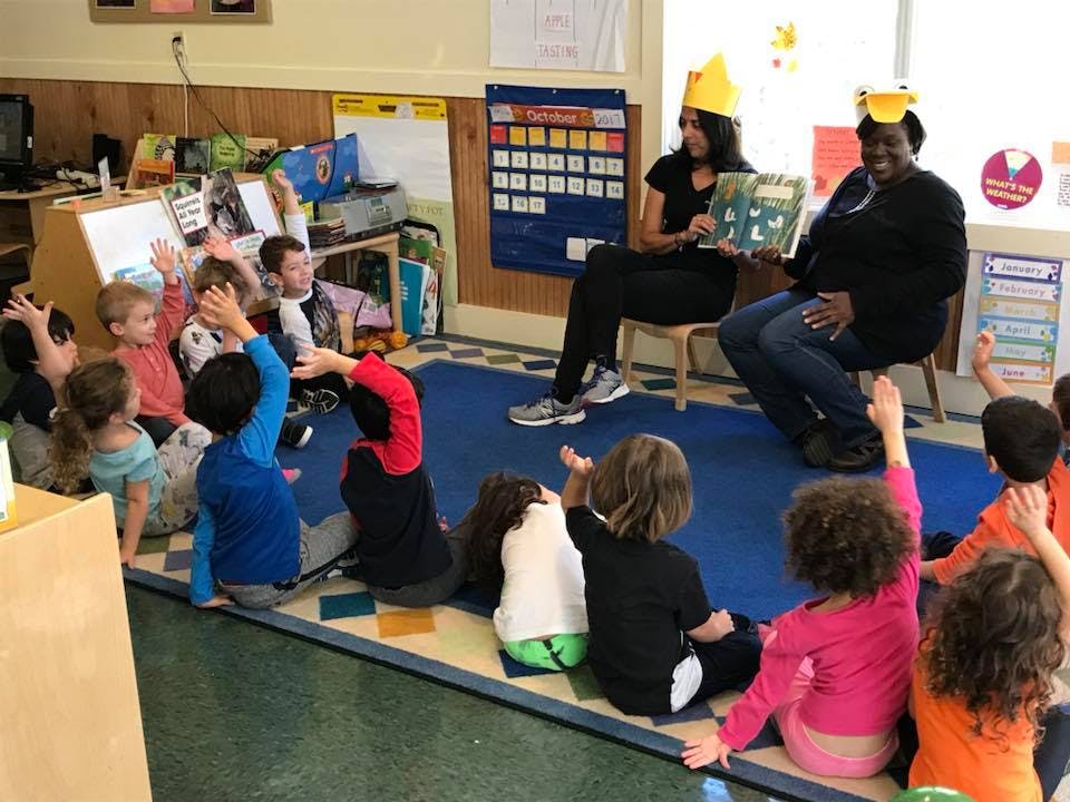 Two people reading a book to a group of children in a classroom