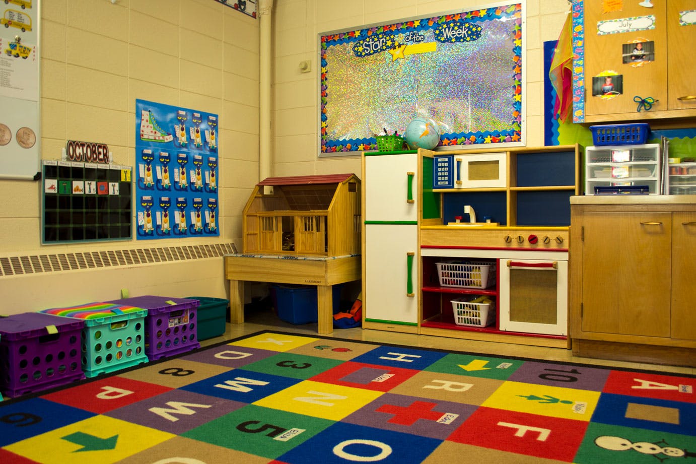Classroom with alphabet rug, play kitchen, and dollhouse