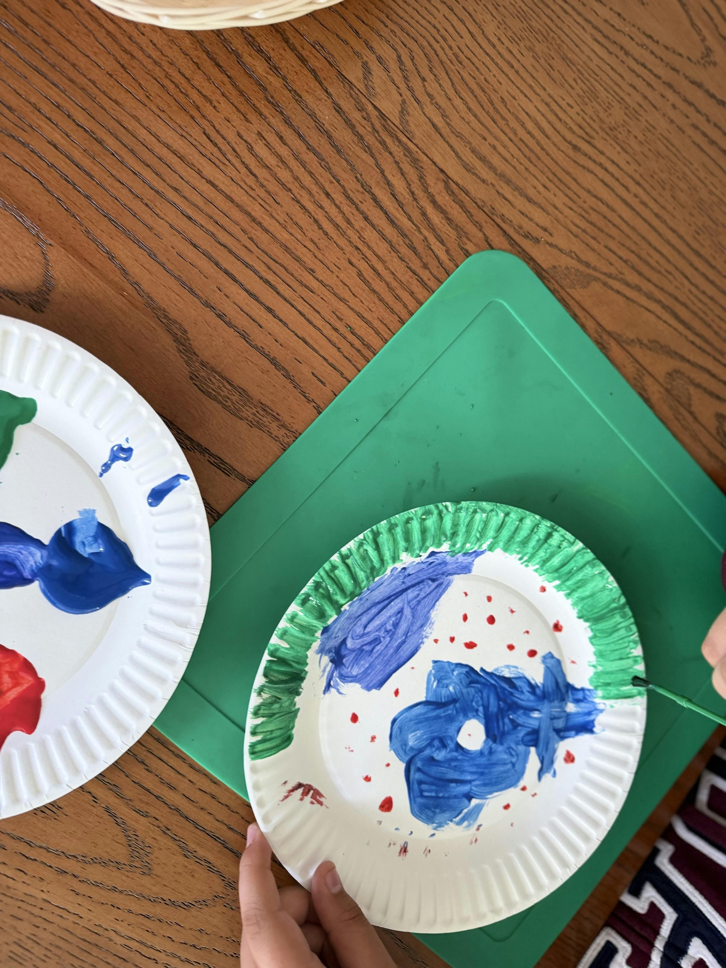 Child painting on a paper plate with blue, green, and red paint