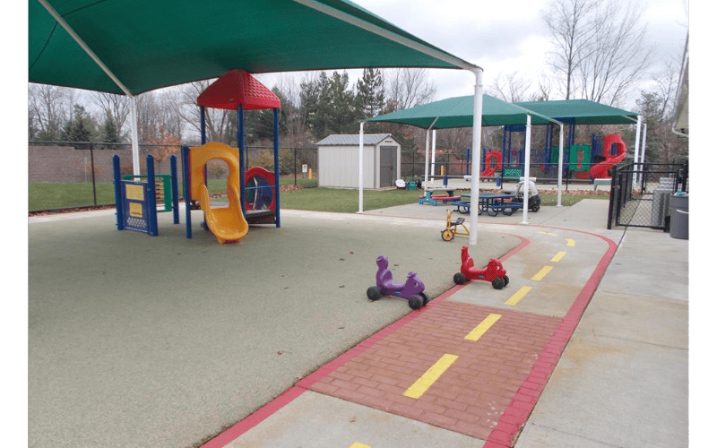 Outdoor playground with colorful play structures and riding toys on a paved path